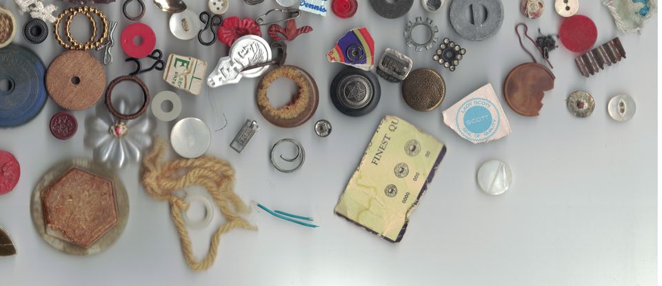 Photograph of about 50 random tiny bits, buttons, hooks, torn corners, snaps and rings and metal whatnots.